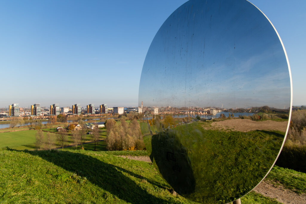 Spiegelkunstwerk op een groene heuvel met uitzicht over Barendrecht