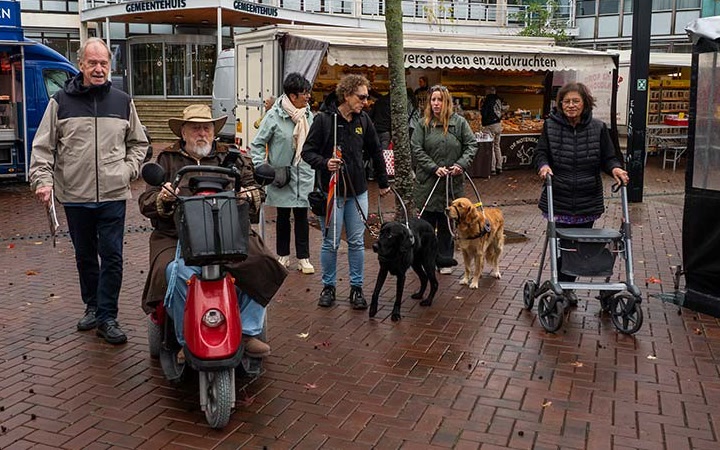 Deelnemers aan de veiligheidsschouw met scootmobiel, rollator en geleidehonden op de markt bij het gemeentehuis van Barendrecht