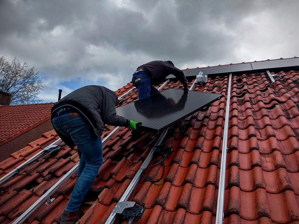 Monteurs plaatsen een zonnepaneel op het dak van een woning.